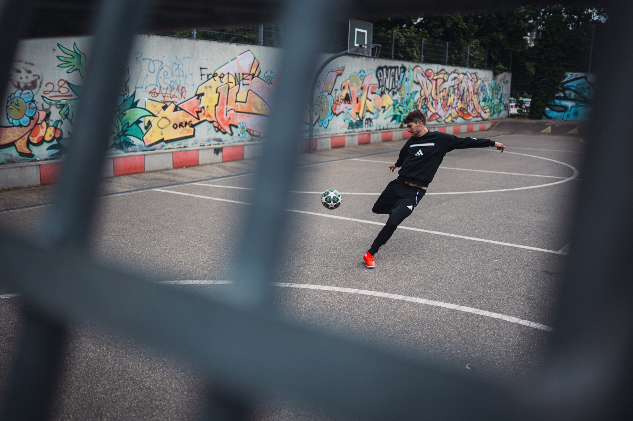 Seen through a fence, a player strikes the Champions League ball on a graffiti-lined street court in Munich.